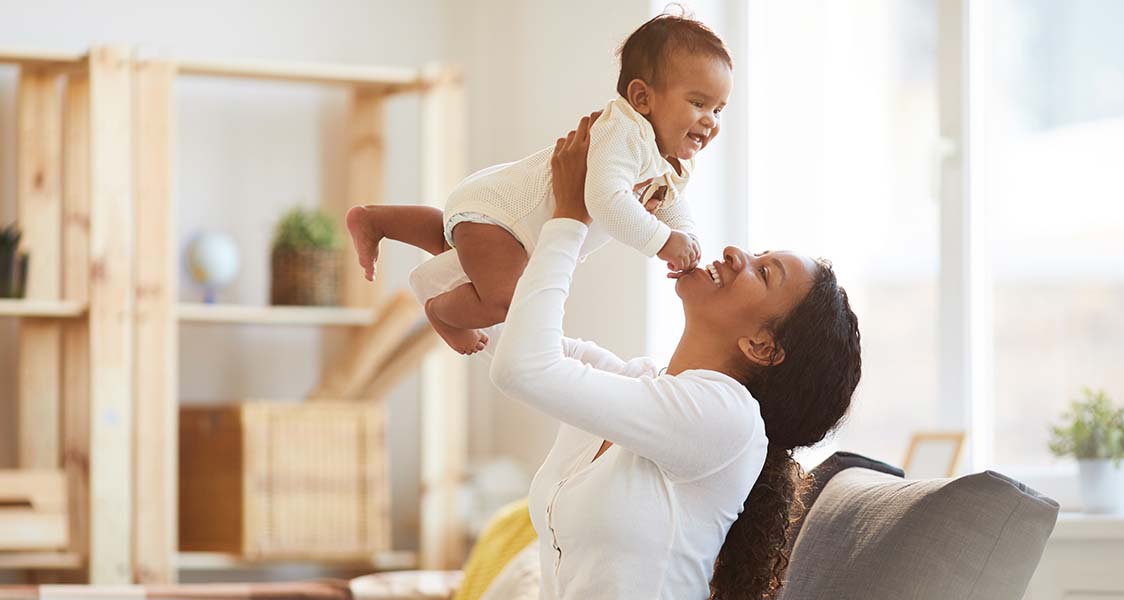Jolly excited young African woman with pony tail enjoying maternity and having fun with baby son at home