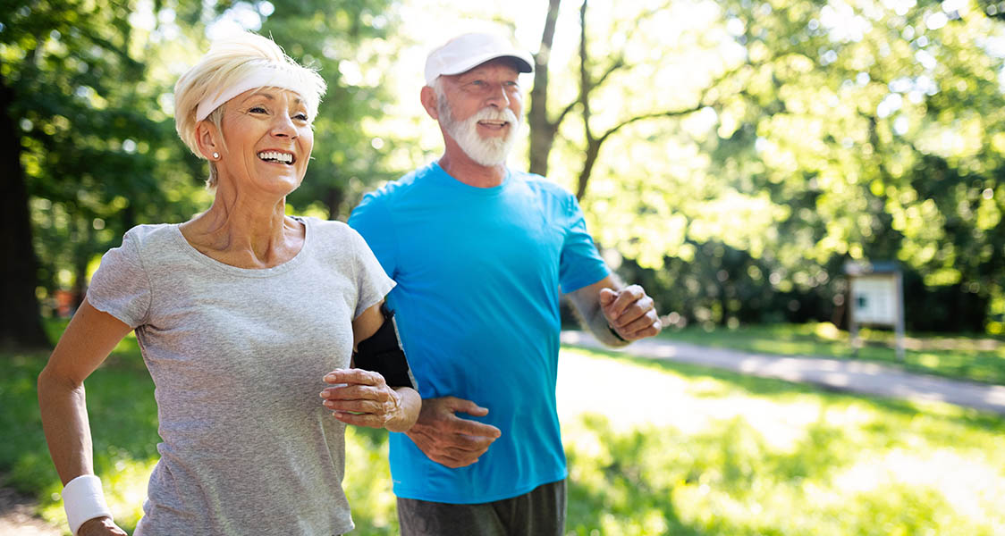 Elderly couple running in a park on a summer day.