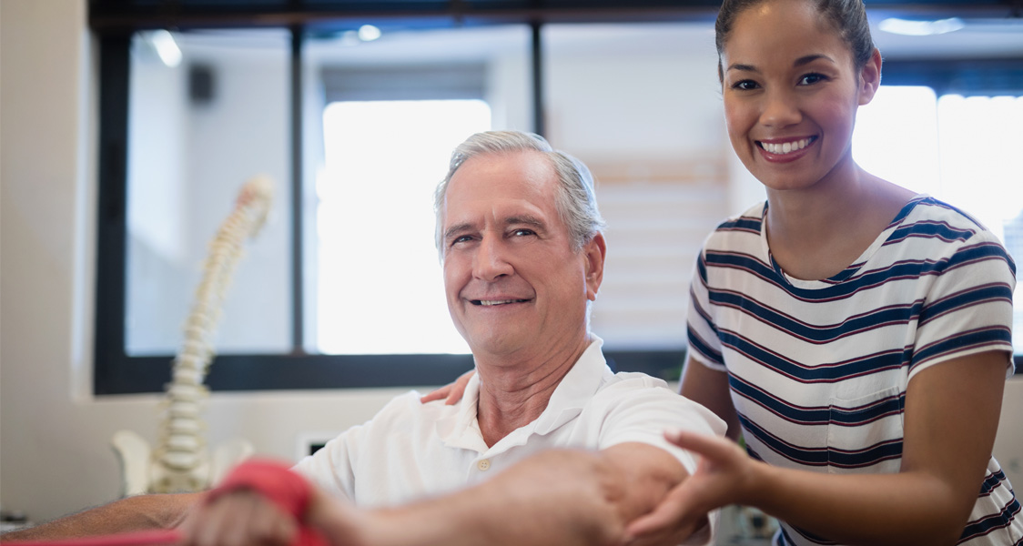 Woman therapist providing stroke rehabilitation to older man.